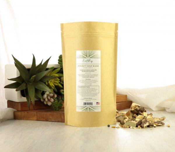 Earthley Immunity Soup Blend tan kraft resealable pouch with burgundy label on rustic surface with green plants