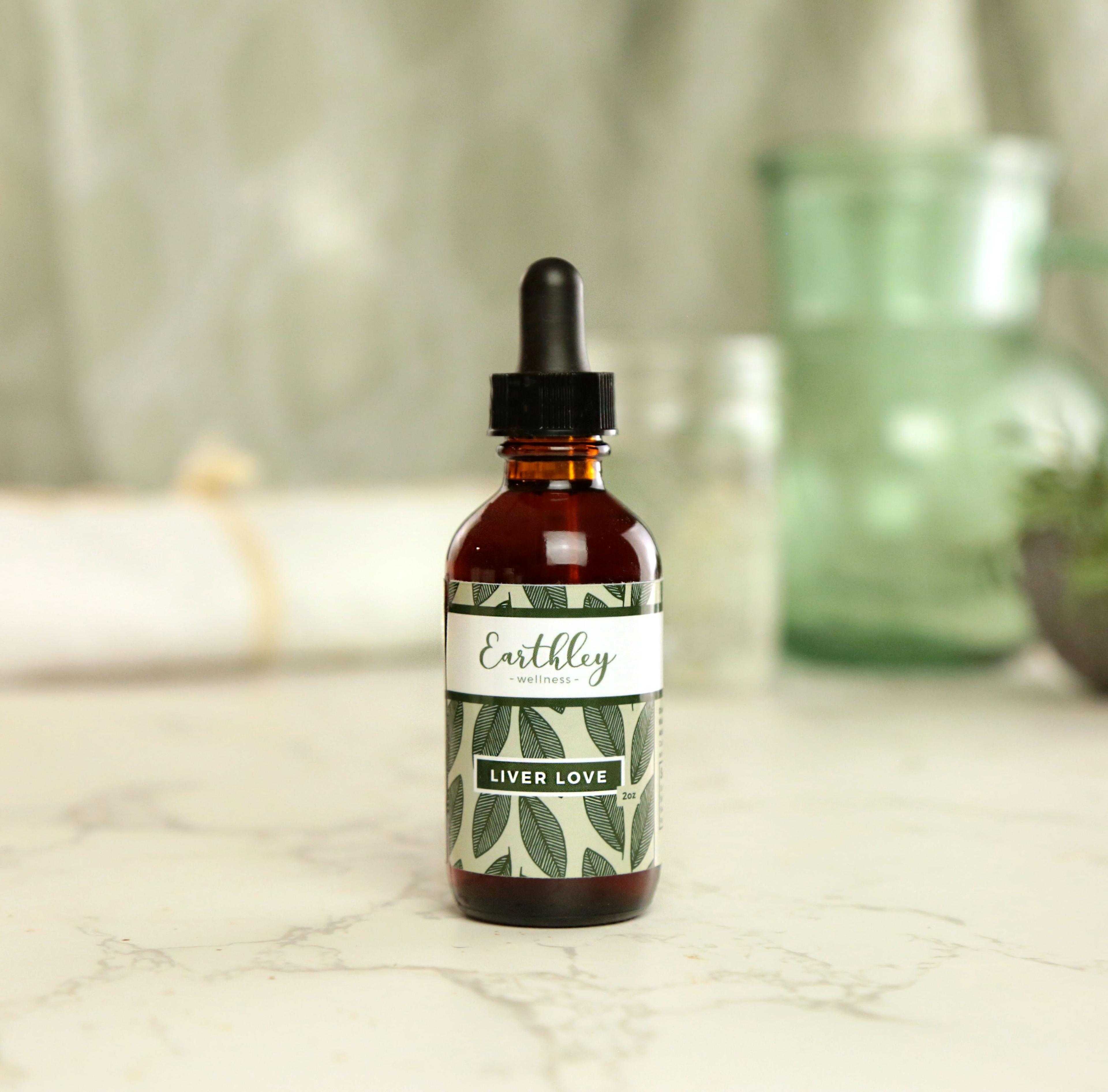 Earthley Liver Love herbal tincture 2oz amber dropper bottle with burgundy leaf pattern label listing burdock root dandelion root and milk thistle seed on marble surface with dried flowers