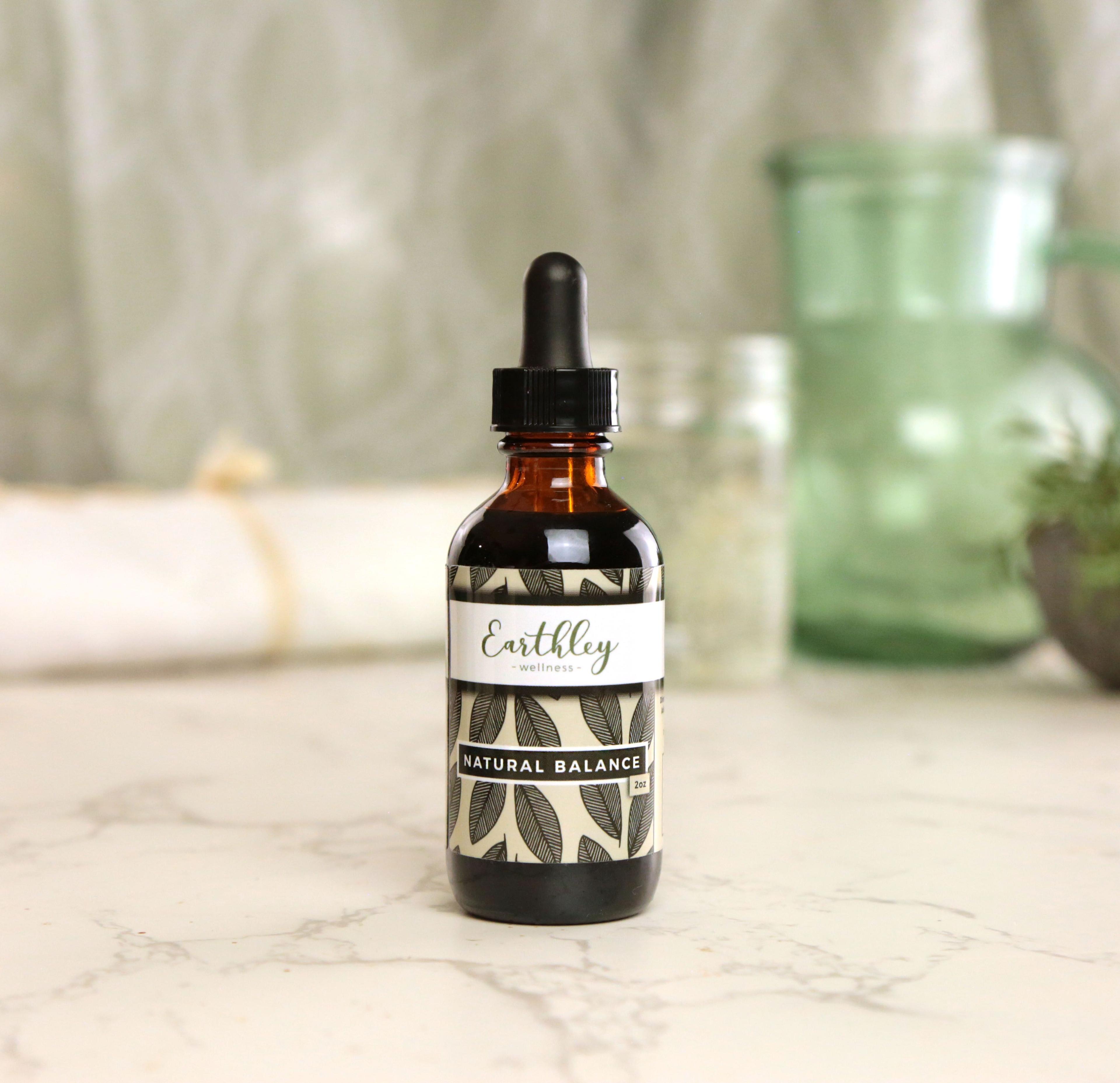 Earthley Natural Balance 4 oz amber dropper bottle with sage green botanical pattern label on marble surface with green glass vase in background