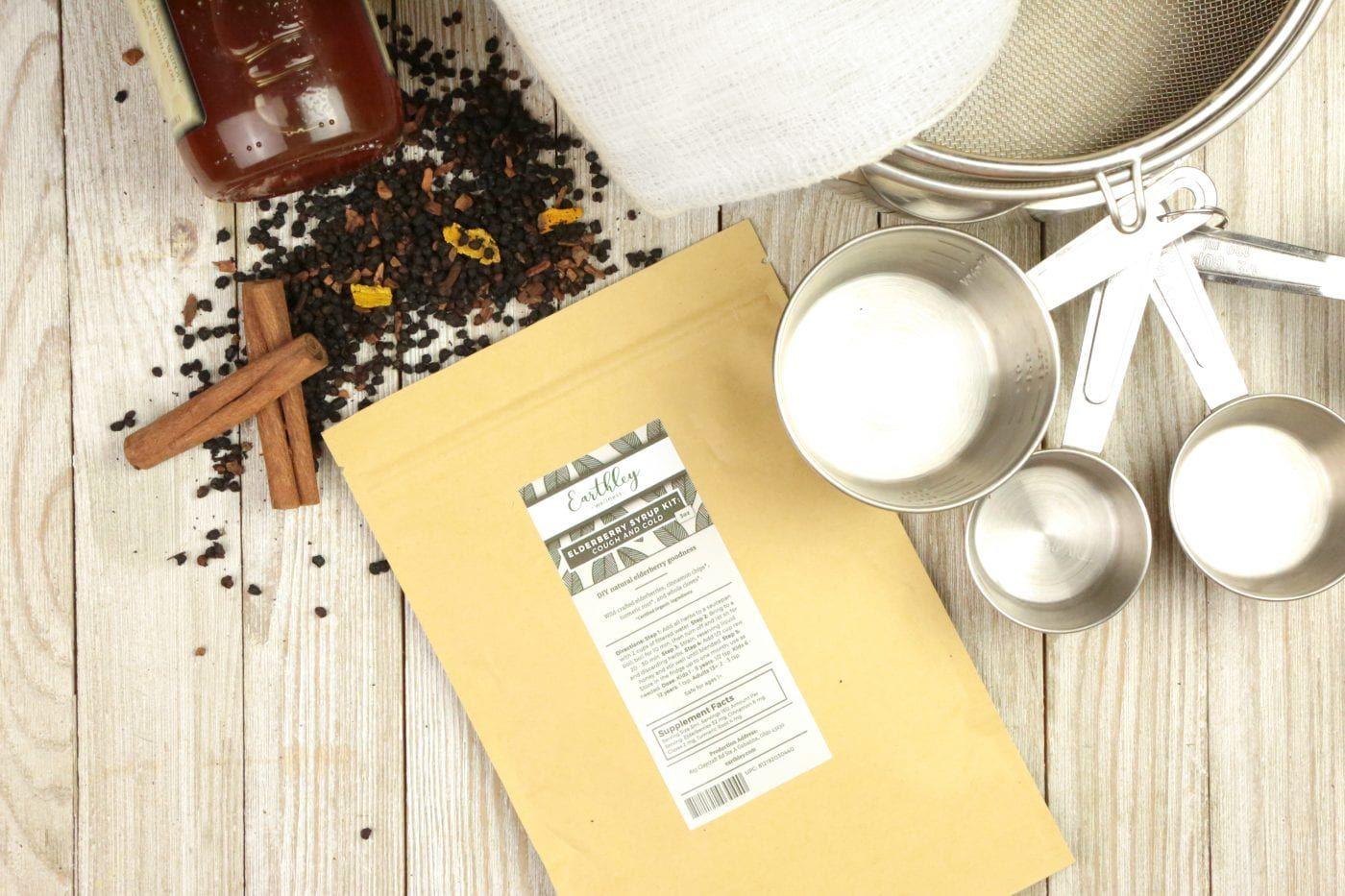 Natural Wellness Classes for Kids Week 4 supplies showing Earthley Elderberry Syrup Kit package with dried elderberries, cinnamon sticks, orange peel, and measuring cups