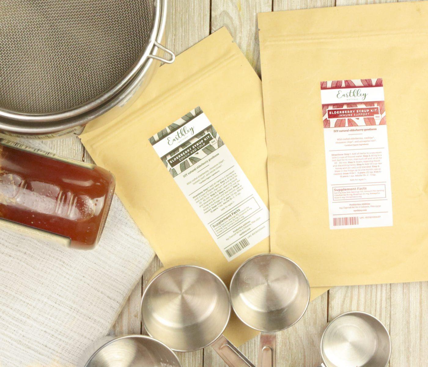 Natural Wellness Classes for Kids Week 1 supplies showing two Earthley Elderberry Syrup Kit packages with measuring cups, strainer, and honey jar