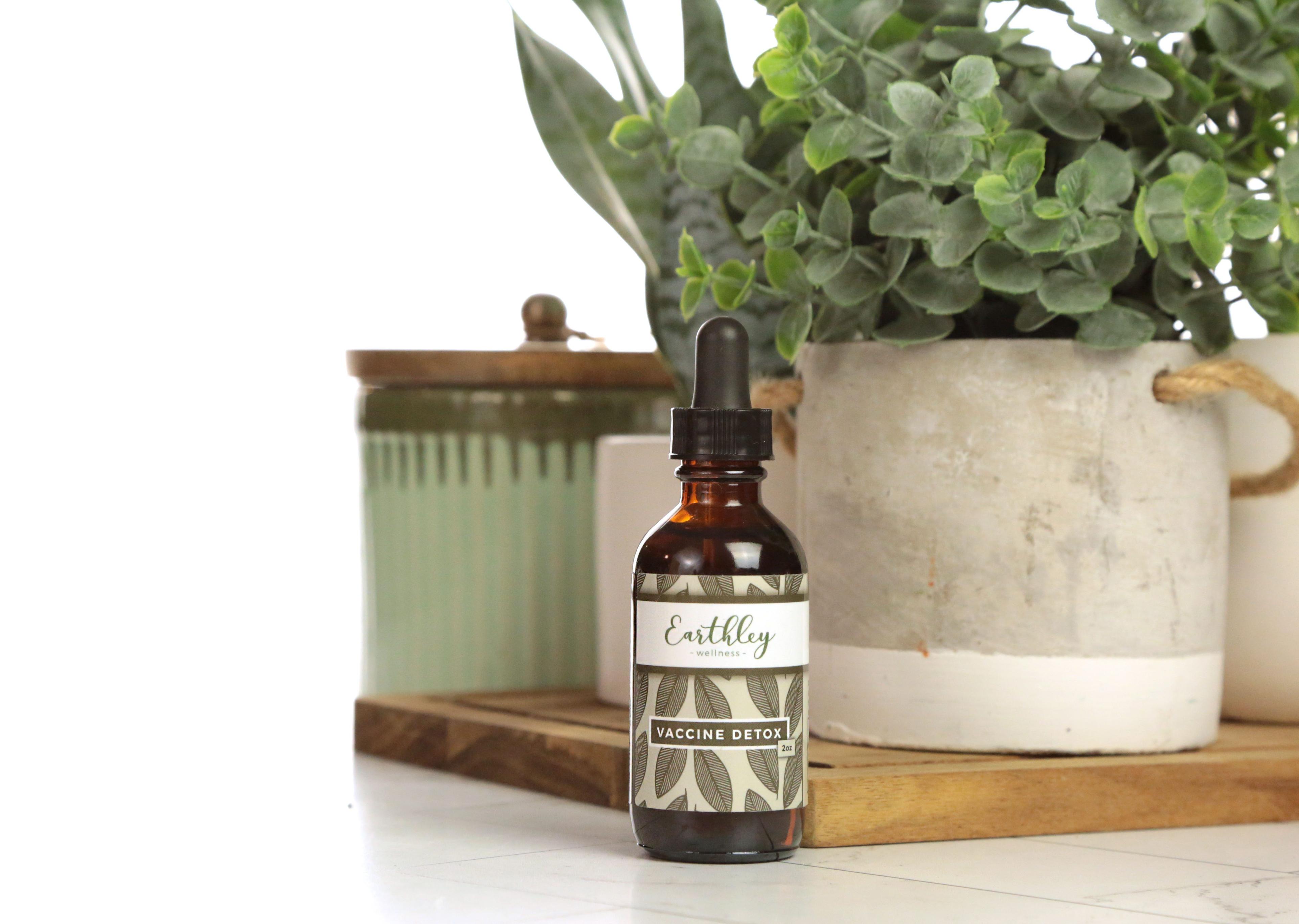 Earthley Vaccine Detox 2oz amber dropper bottle with leaf pattern label displayed with plants and decorative containers