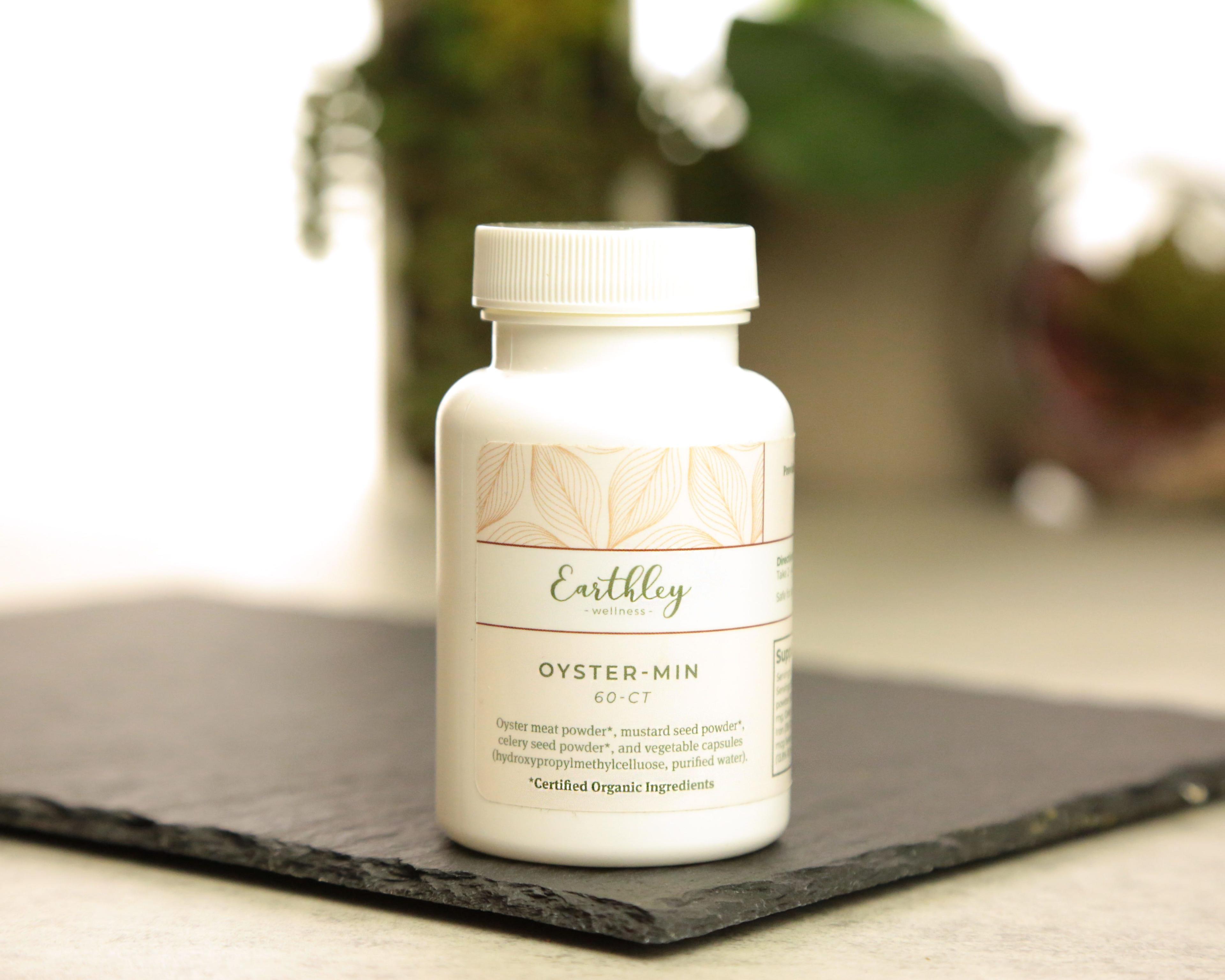 Earthley Oyster-Min 60 count white plastic bottle with white lid and cream tan leaf pattern label on dark gray slate surface with green plant in background