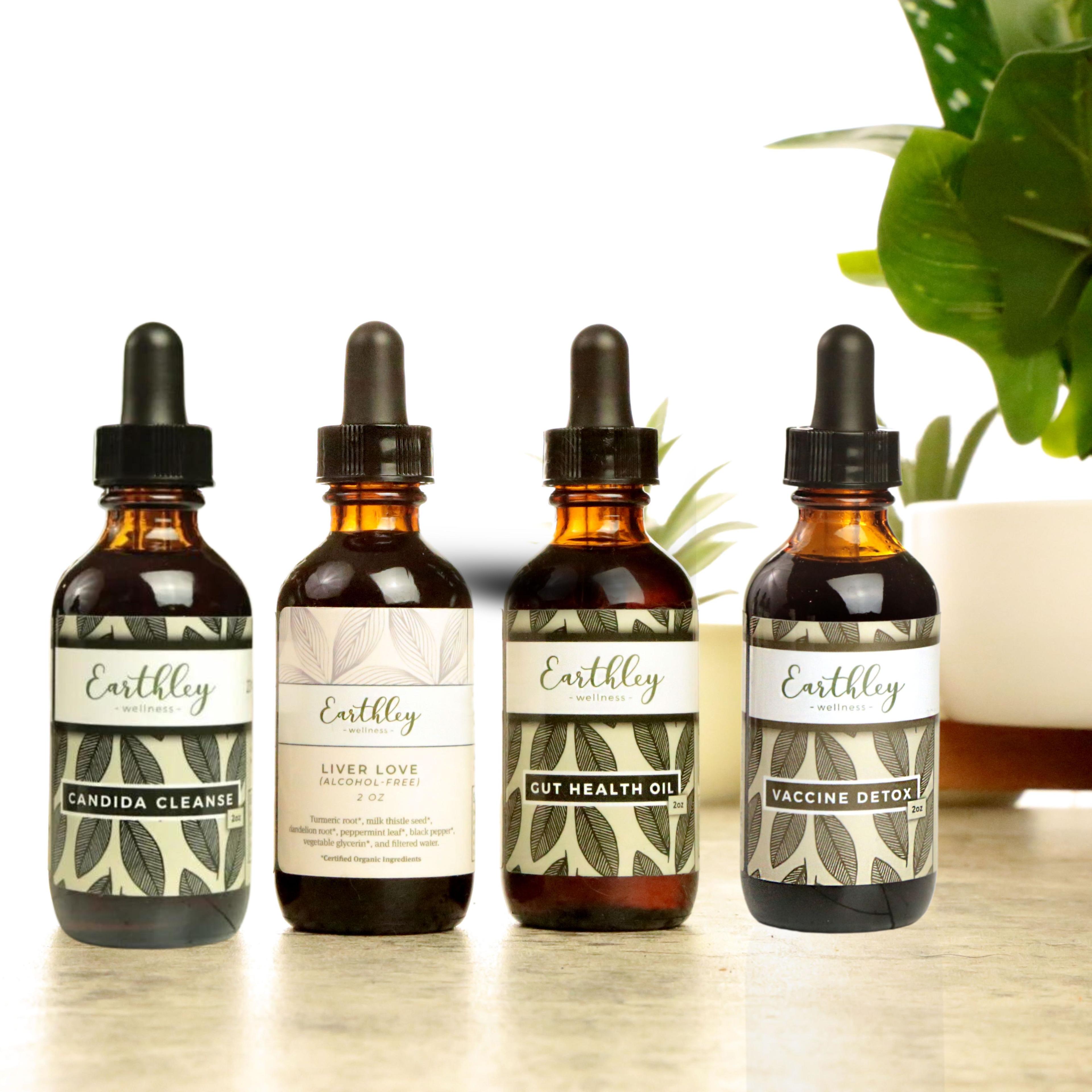 Earthley Parasite Detox Bundle with four amber glass dropper bottles showing Candida Cleanse Liver Love Gut Health Oil and Vaccine Detox with sage green leaf labels on tan surface with green plants