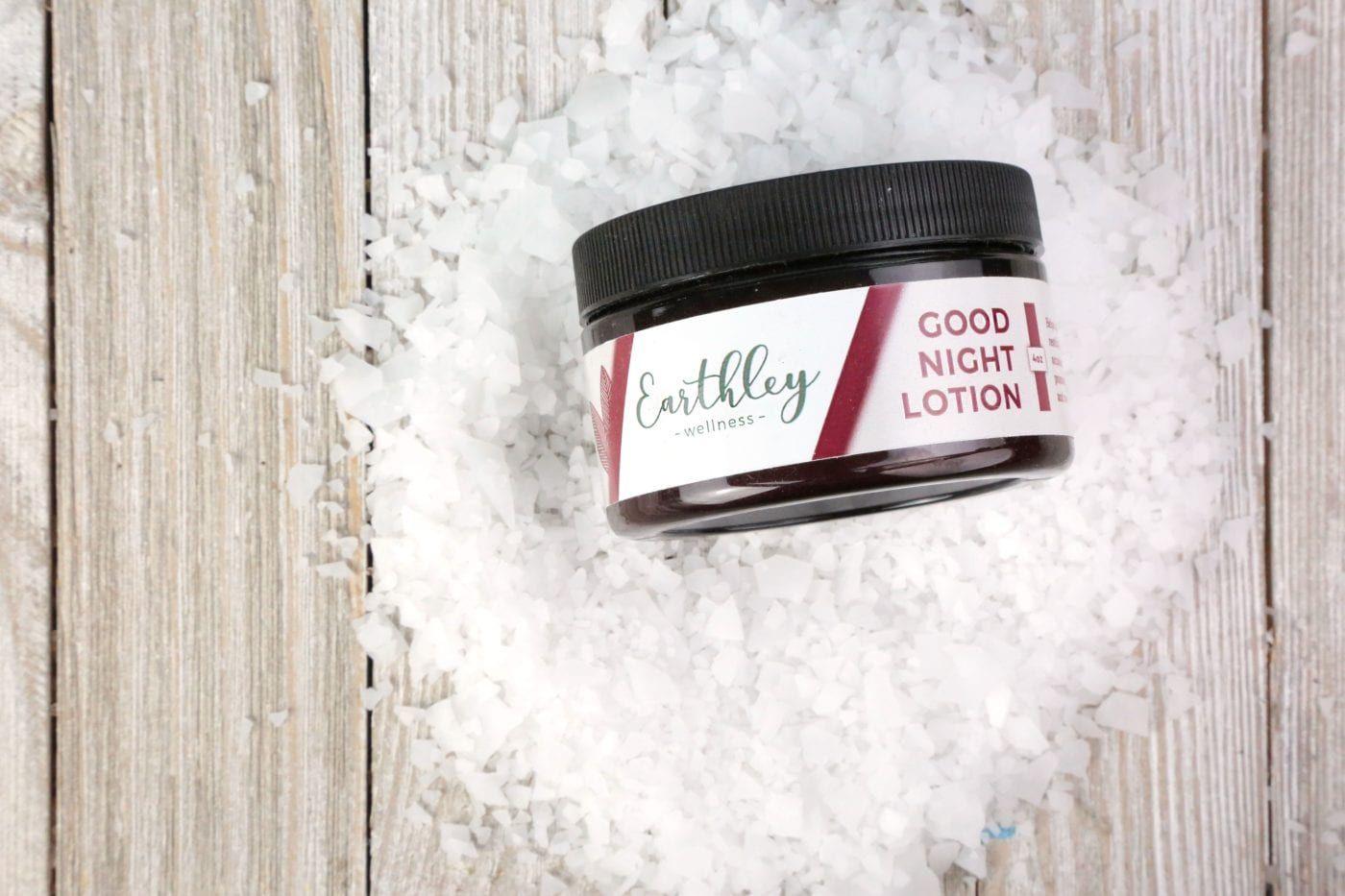 Earthley Good Night Lotion jar with burgundy label on wood surface surrounded by magnesium salt flakes