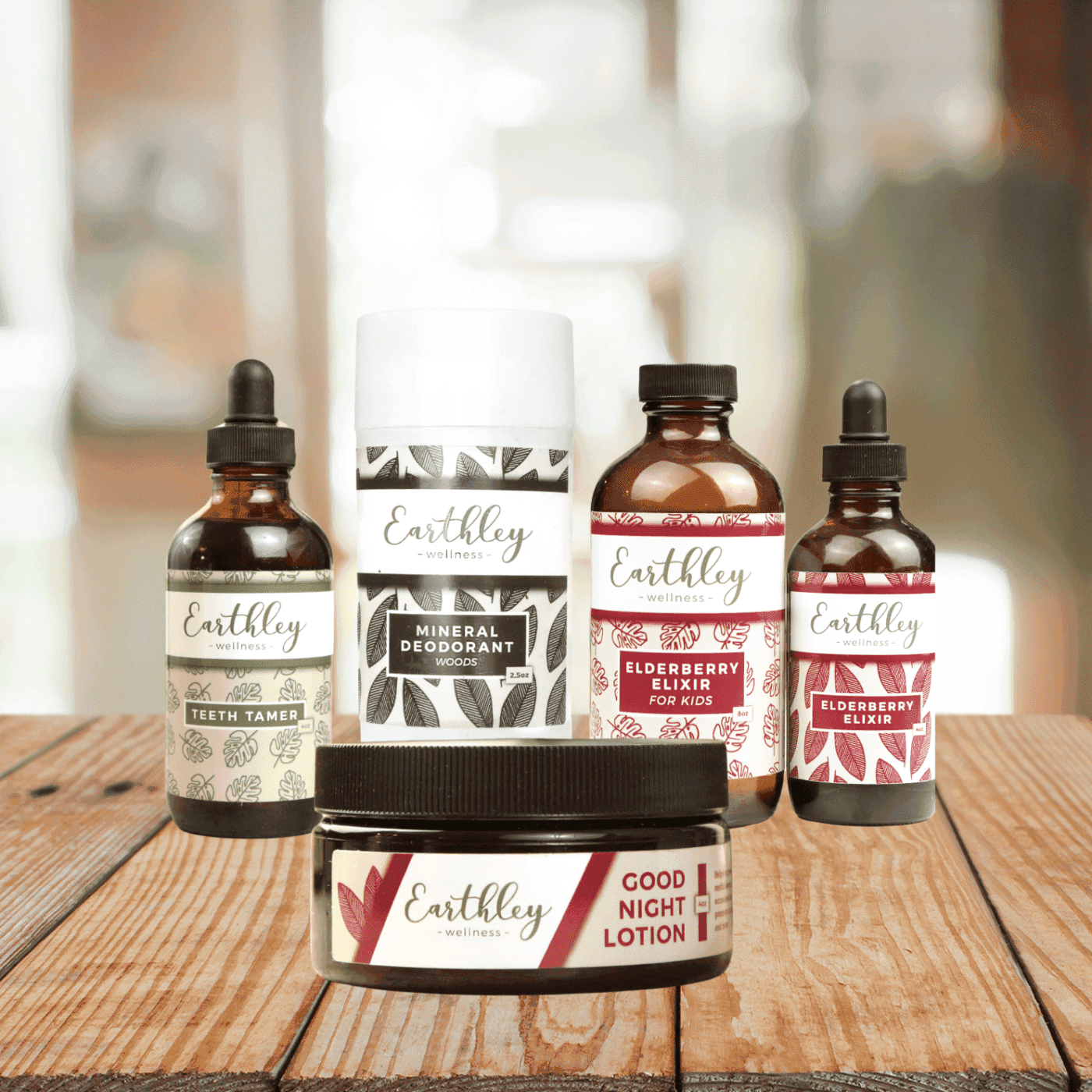 Earthley Retail Wholesaler Bundle featuring amber glass dropper bottles white mineral deodorant tube amber Good Night Lotion jar and various products with burgundy coral and brown leaf pattern labels on wooden surface