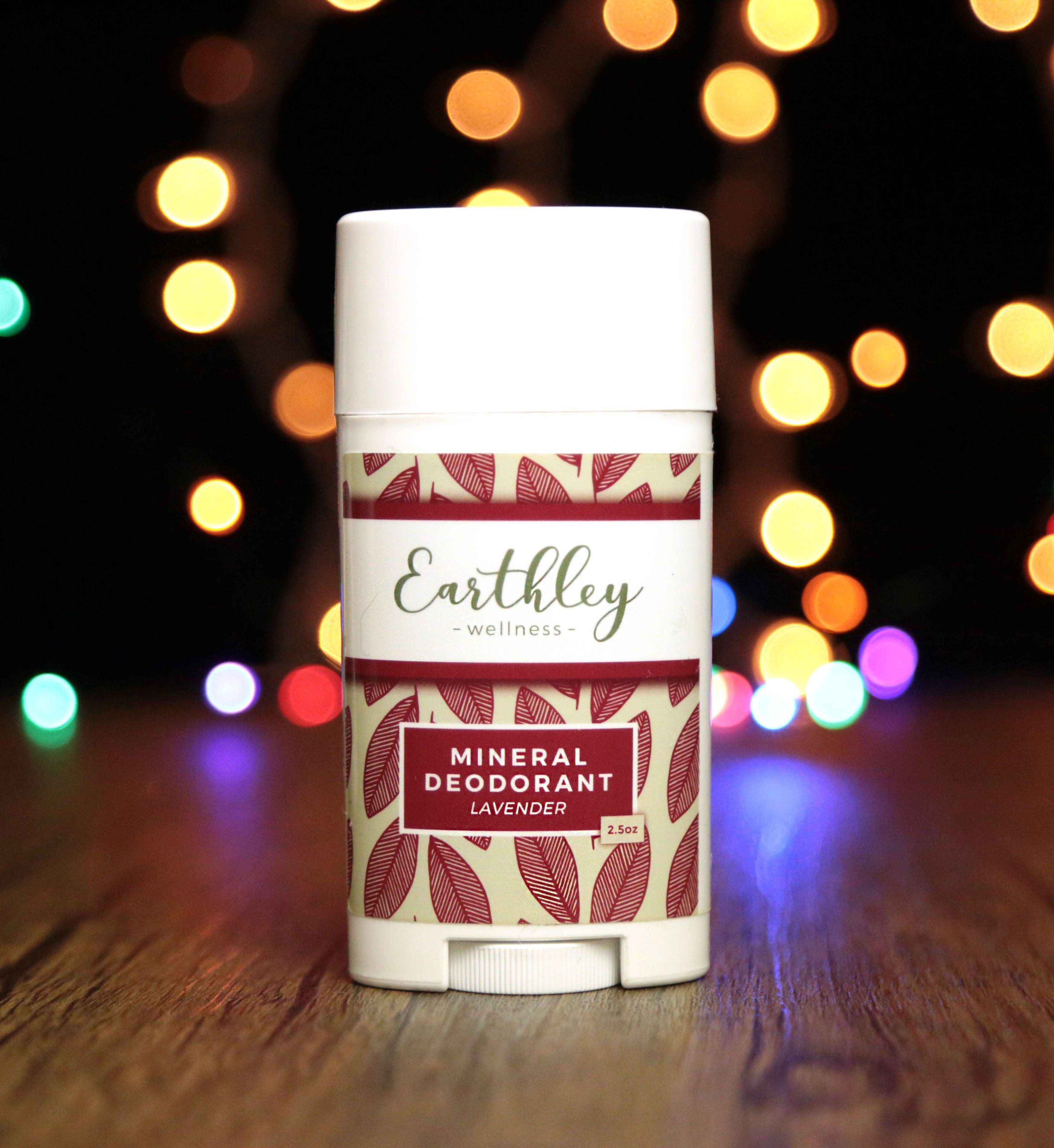 Earthley Mineral Deodorant Lavender 2.5oz white twist-up tube with burgundy red leaf pattern label on dark wooden surface with colorful rainbow bokeh lights in background