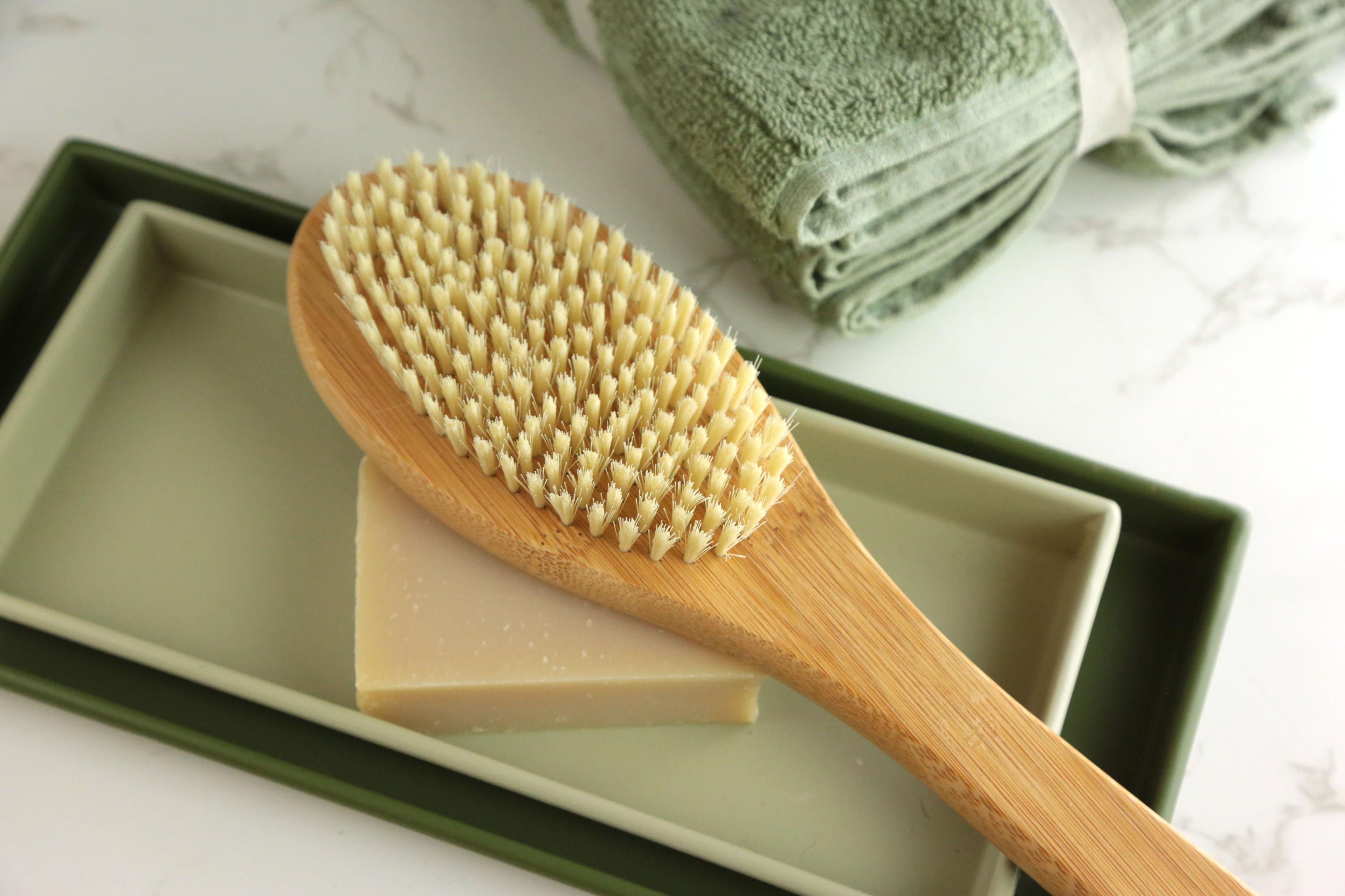 Earthley dry body brush full length view with long wooden handle and oval bristle head for dry brushing on marble surface