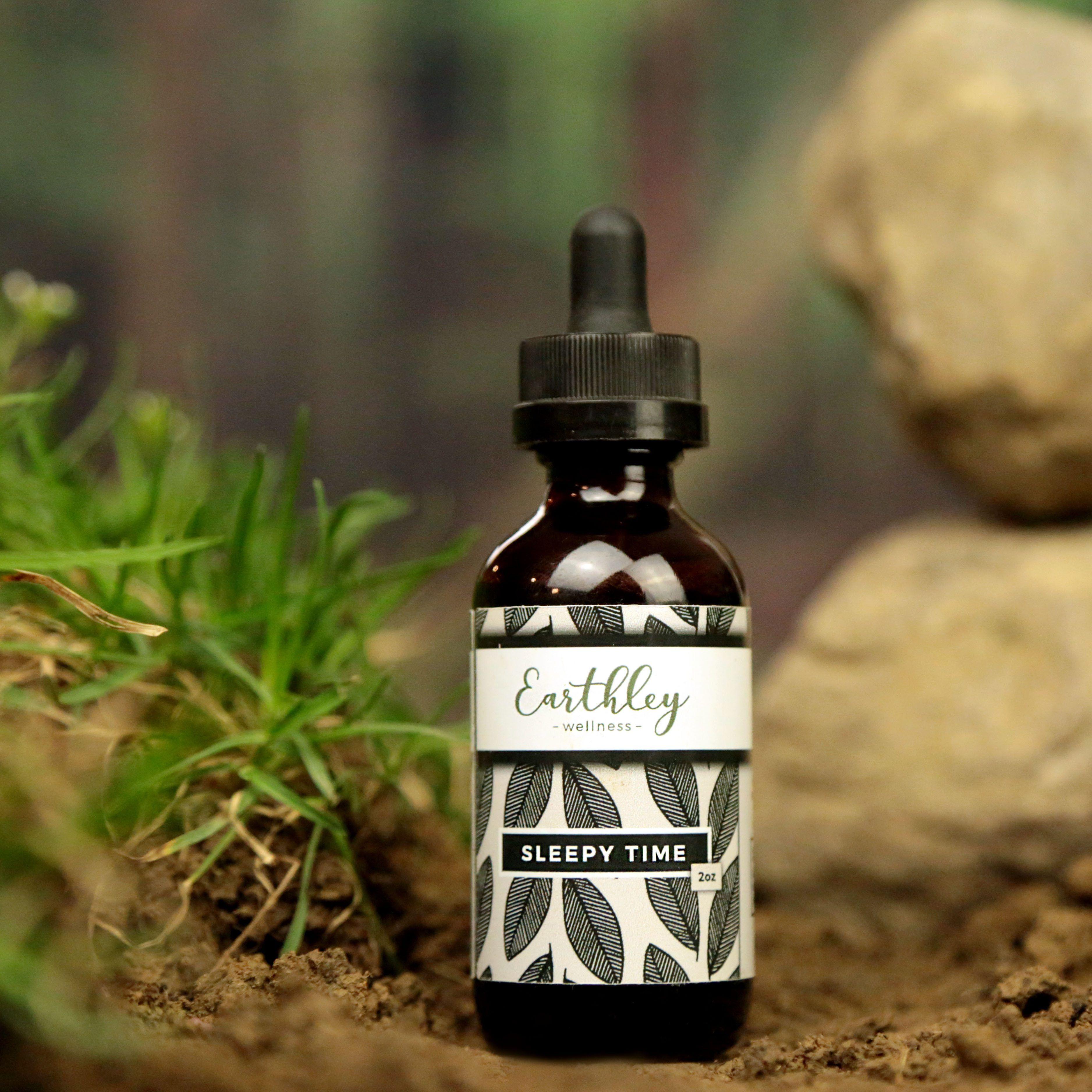 Earthley Sleepy Time 2oz amber dropper bottle with black leaf pattern label in natural outdoor setting with moss and grass