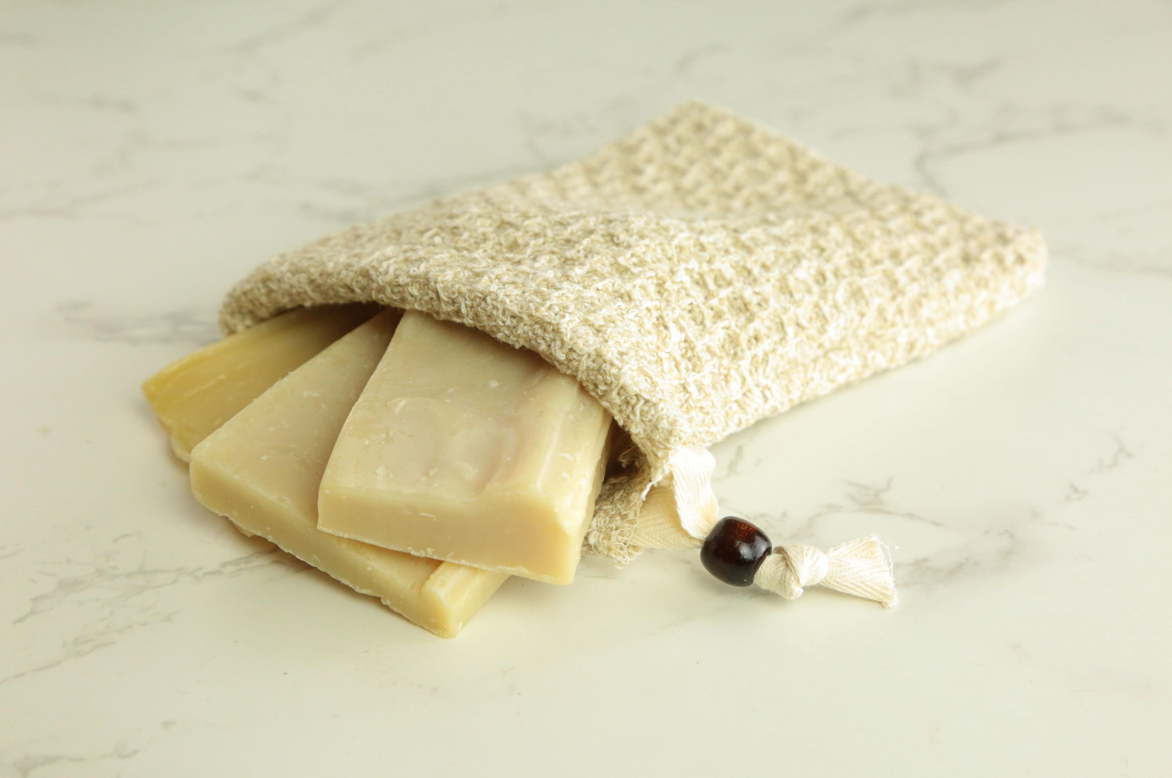 Earthley Soap Pouch with cream natural sisal exfoliating bag containing pale yellow soap bar scraps with brown wooden bead closure on white marble