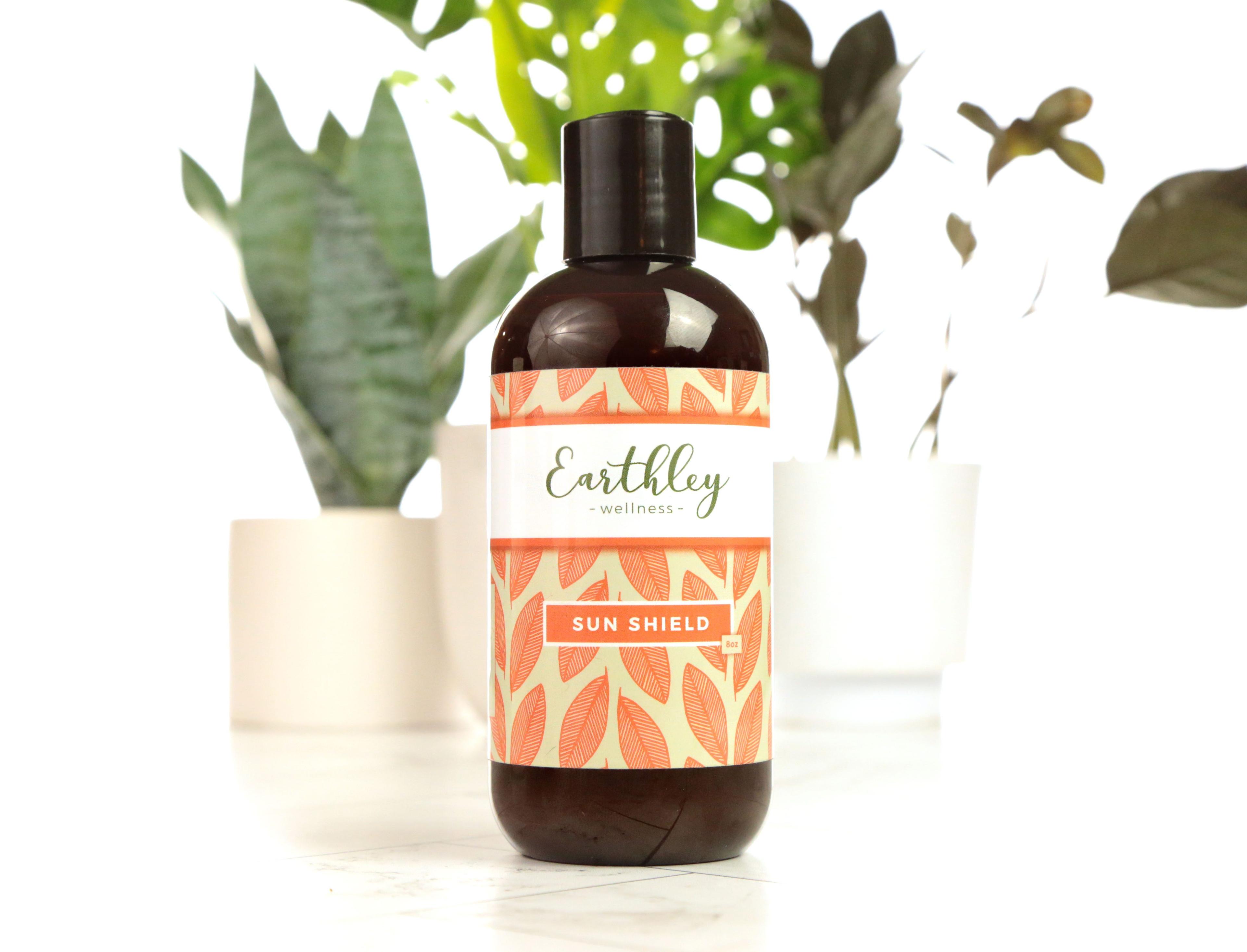 Earthley Sun Shield lotion bottle with orange leaf pattern label and houseplants in background