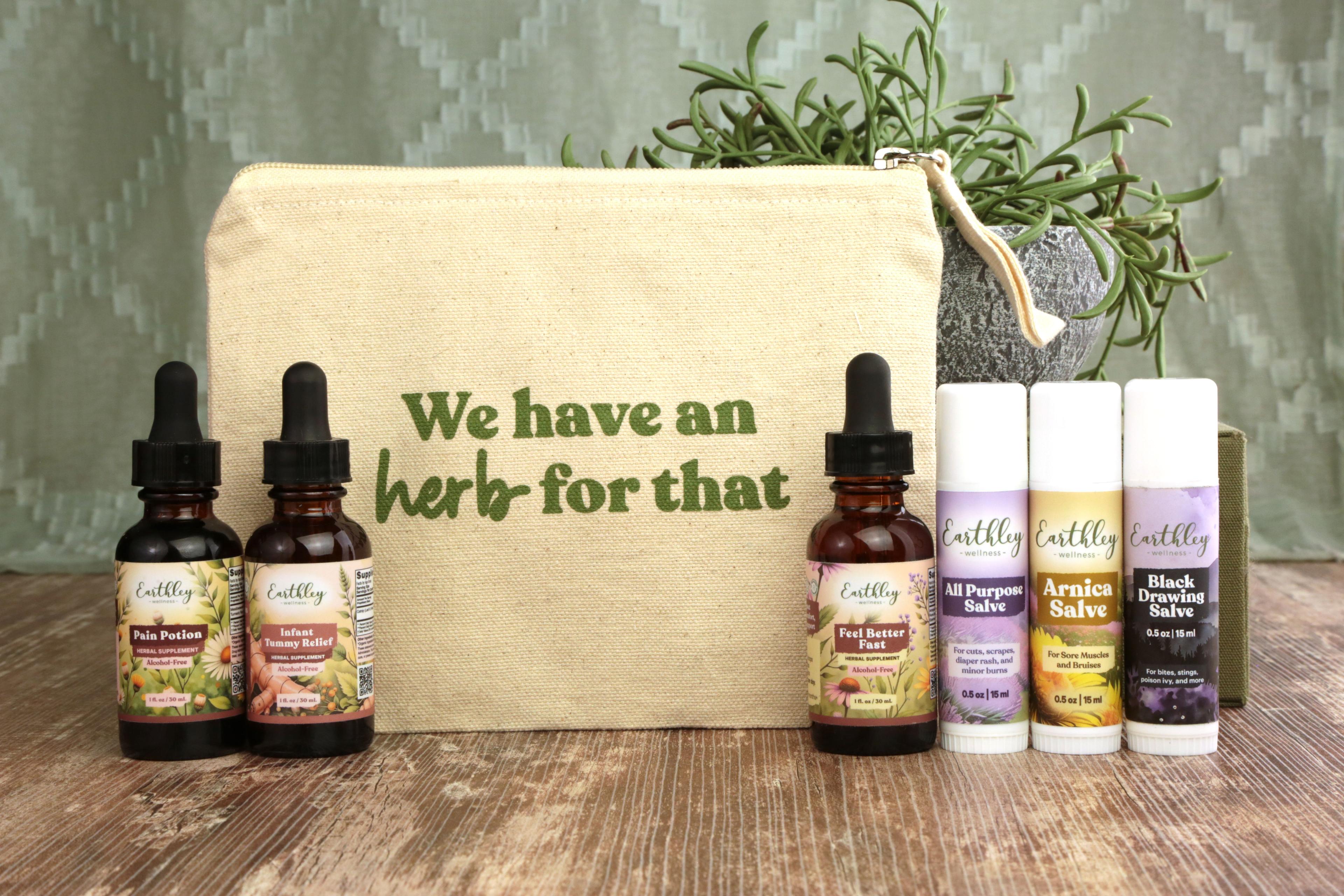 Earthley Tincture Bag Bundle with We have an herb for that natural cream canvas pouch three amber dropper bottles and three white salve tubes with purple labels on rustic brown wooden surface