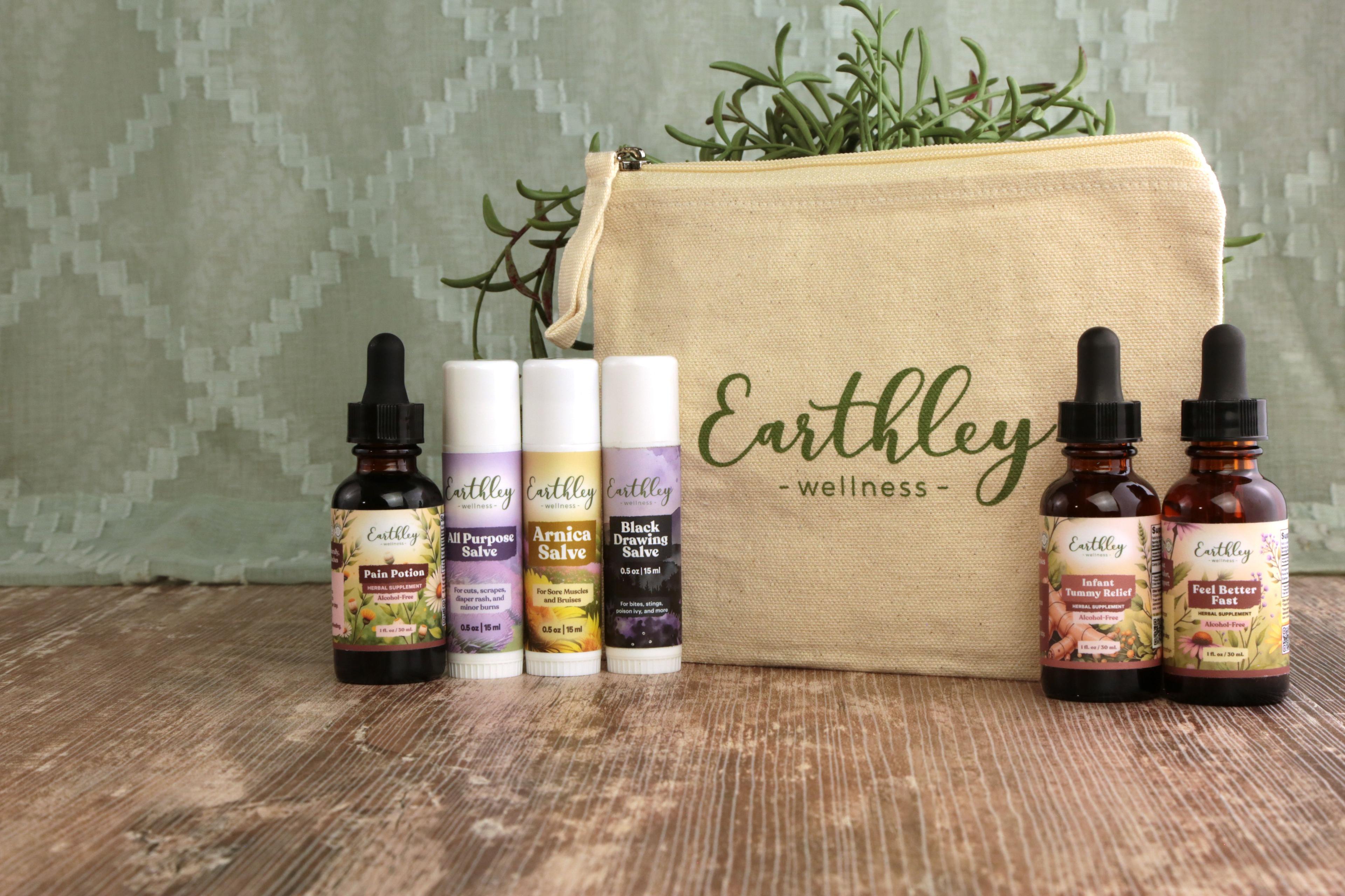 Earthley Tincture Bag Bundle with natural cream canvas pouch amber dropper bottles with purple and yellow floral labels white salve tubes and green rosemary on rustic brown wooden surface