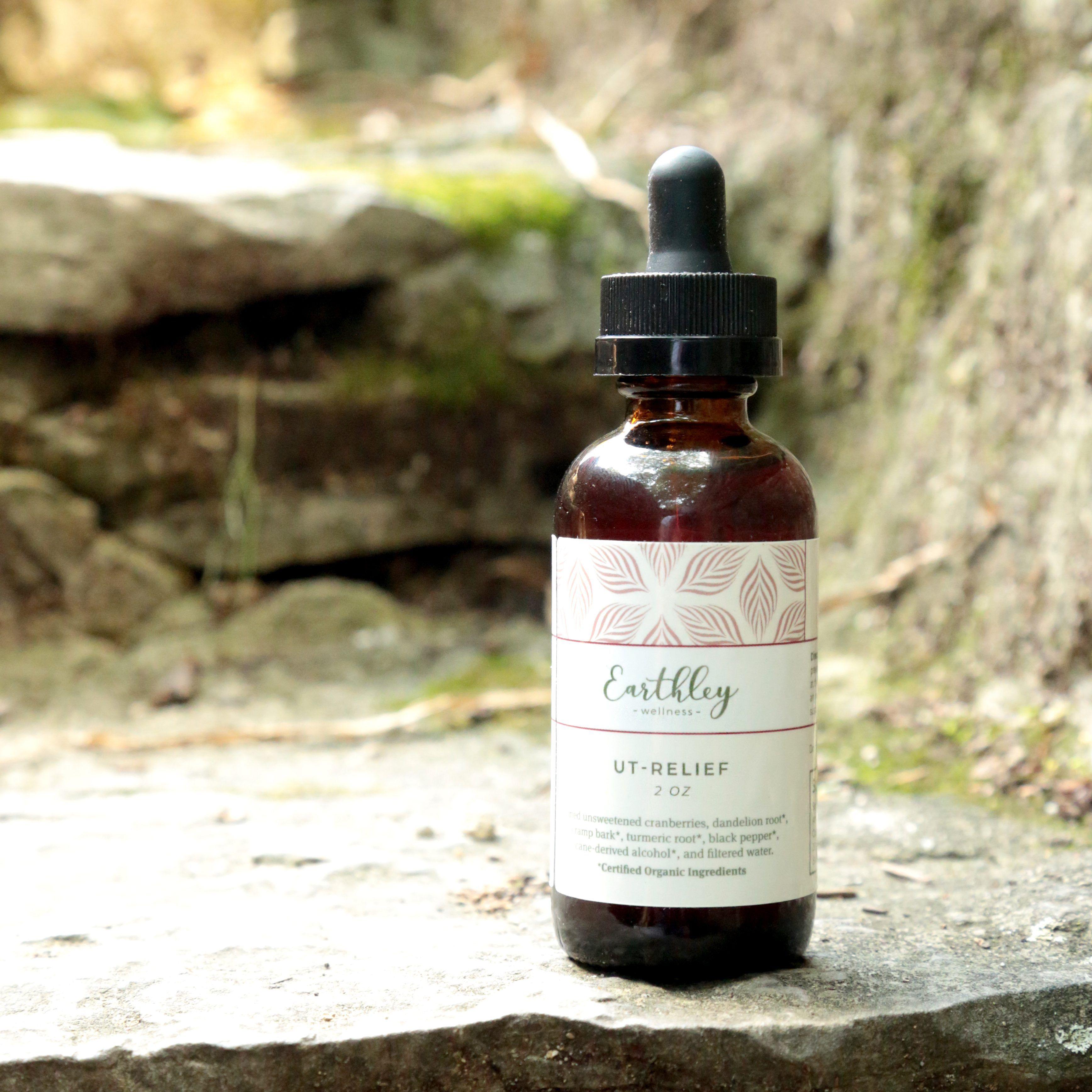 UT-Relief 2oz herbal extract in amber dropper bottle with pink leaf label on natural stone in outdoor forest setting