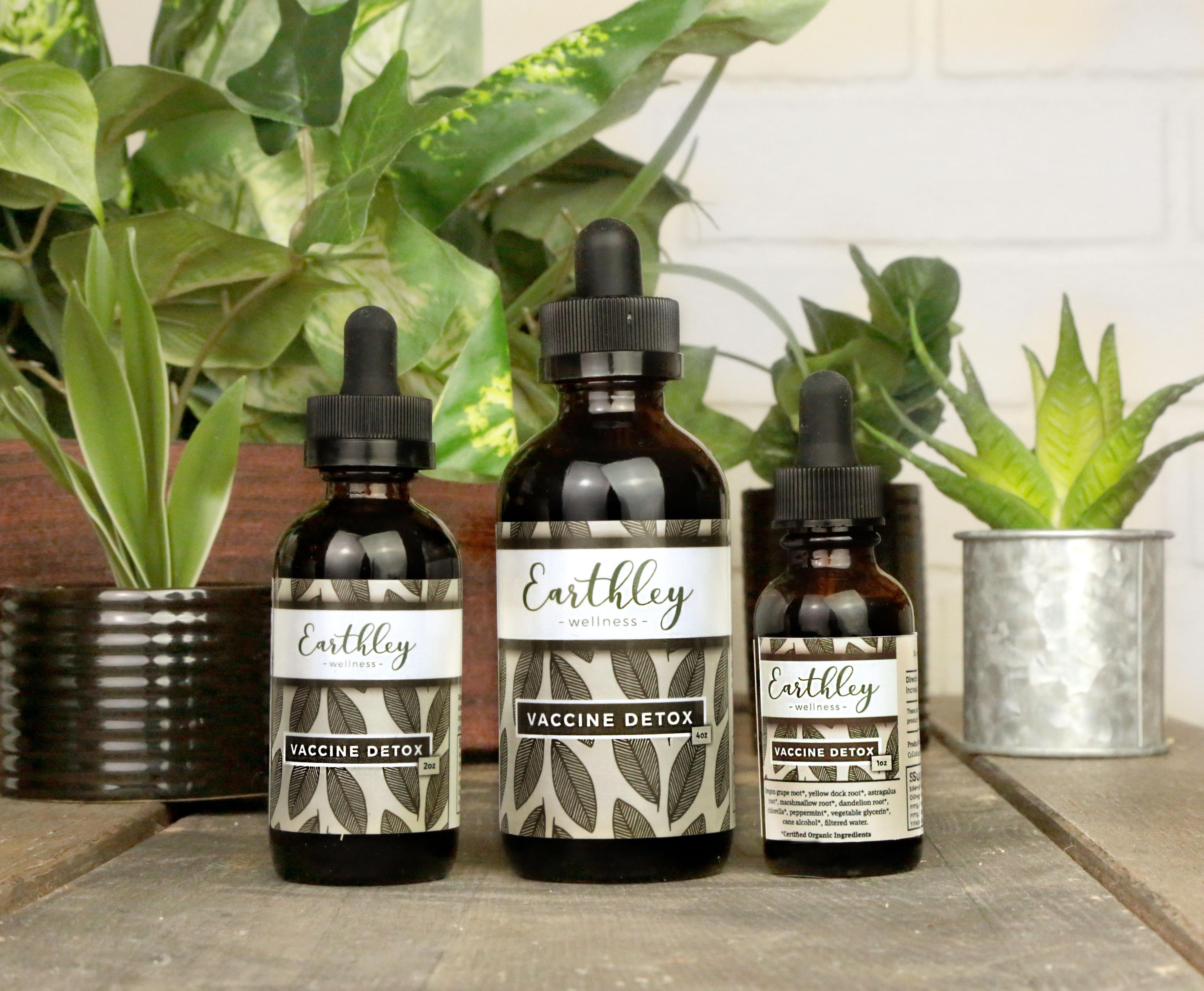Three Vaccine Detox tincture bottles in different sizes with dark green leaf pattern labels on wooden crate with plants