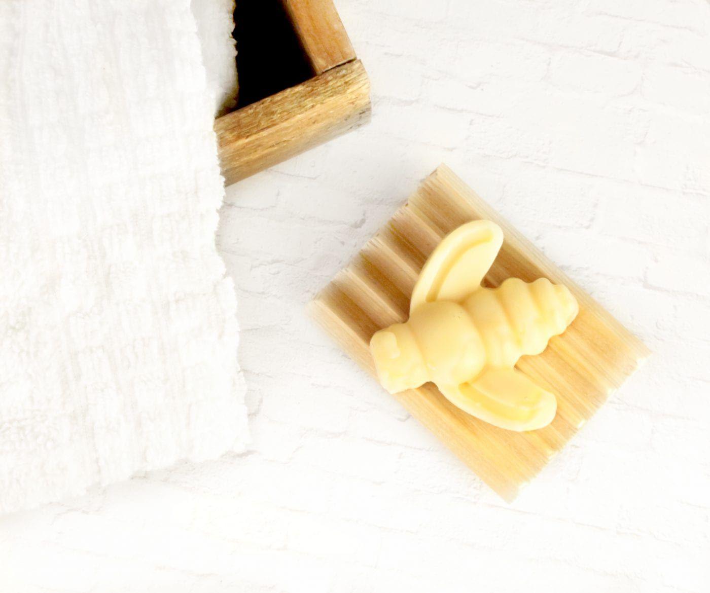 Bee-shaped natural soap bar on bamboo wooden soap dish with white towel
